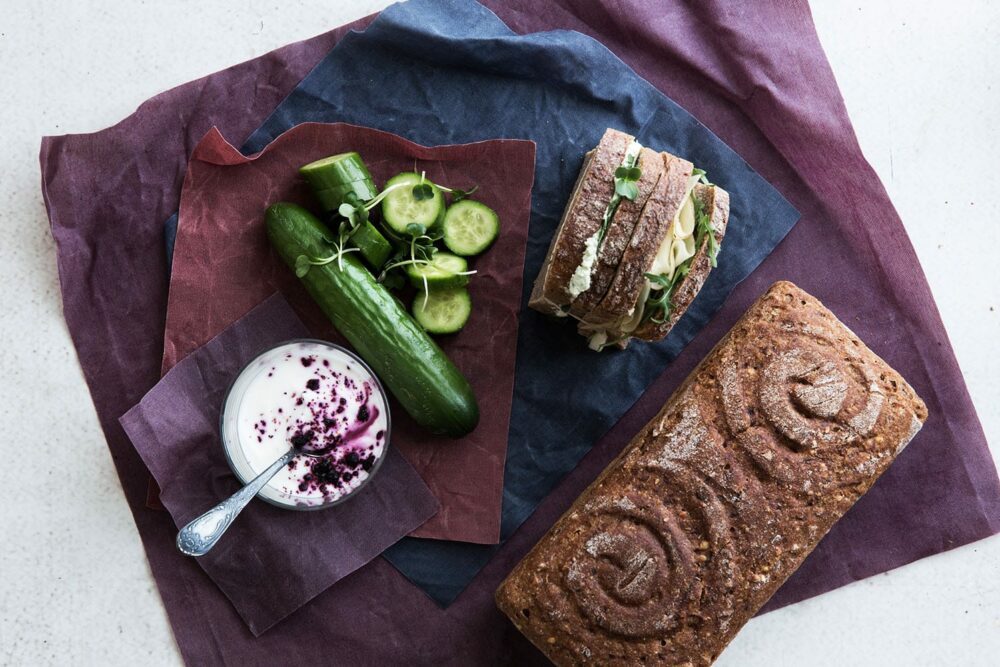 Ein Glas, eine Gurke und eine Schnitte sowie ein Brot liegen auf Bienenwachstücher