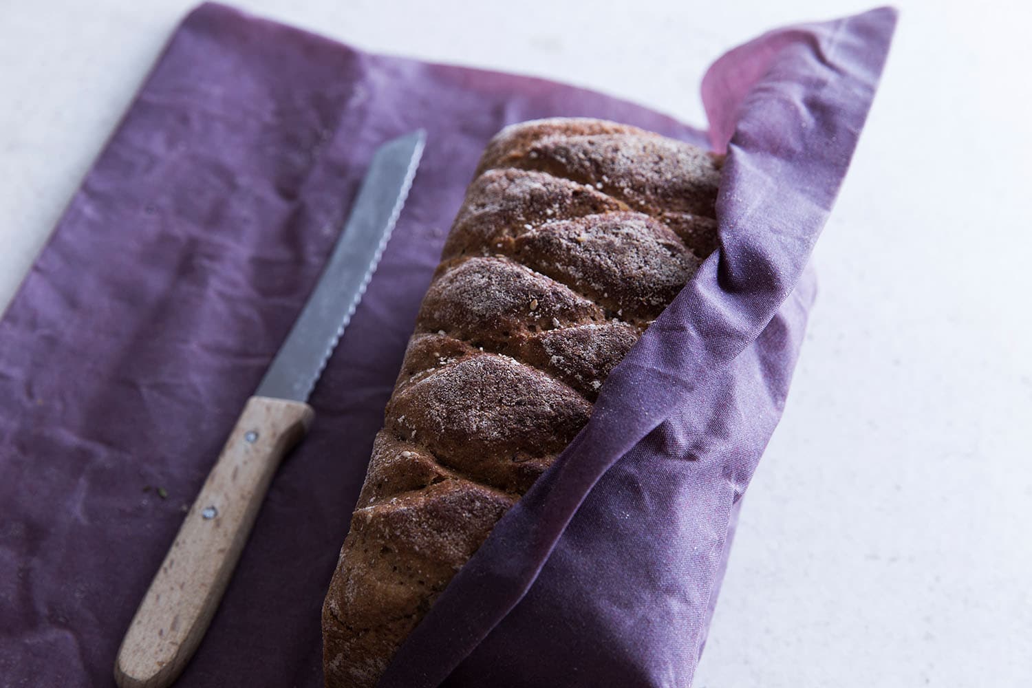 Brot eingepackt in einem Bienenwachstuch in der Farbe Lila, daneben liegt ein Messer.