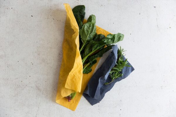 Two yellow and blue beeswax wraps filled with spinach leaves and rosemary.